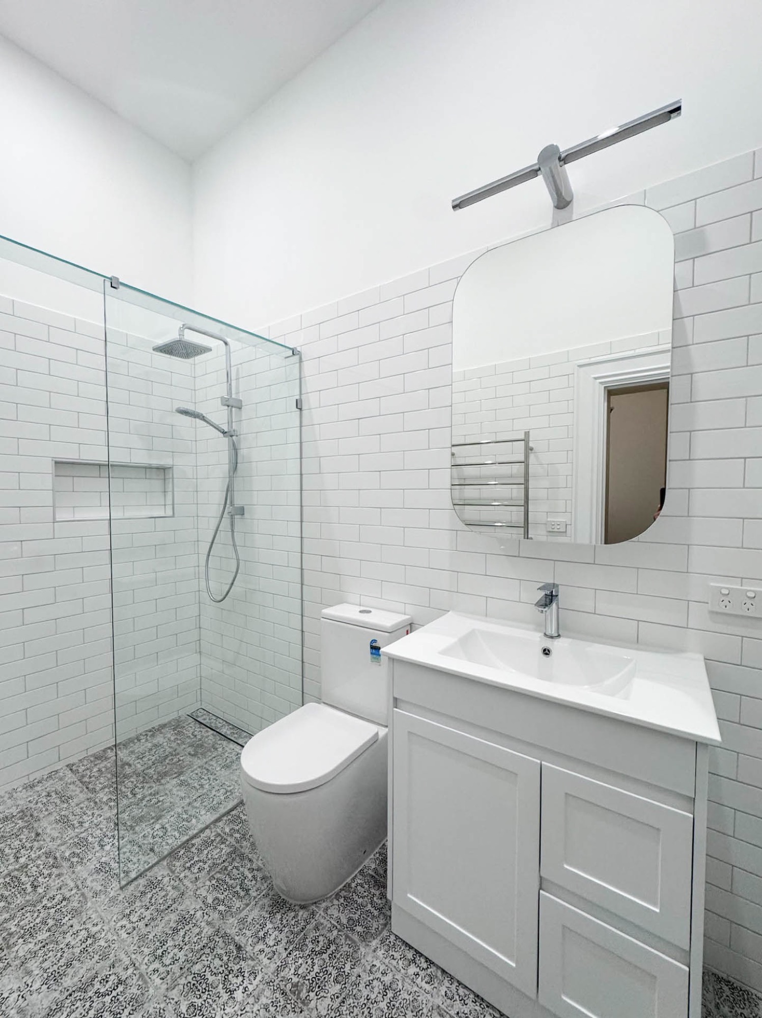 Completed bathroom with walk-in shower, toilet, vanity and patterned floor tiles