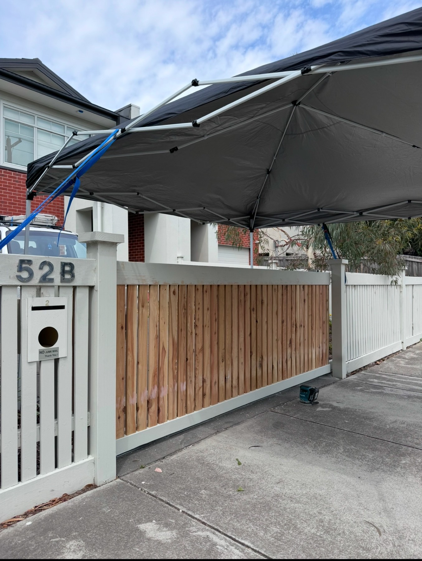 Custom timber sliding gate installation continuing beneath temporary rain protection