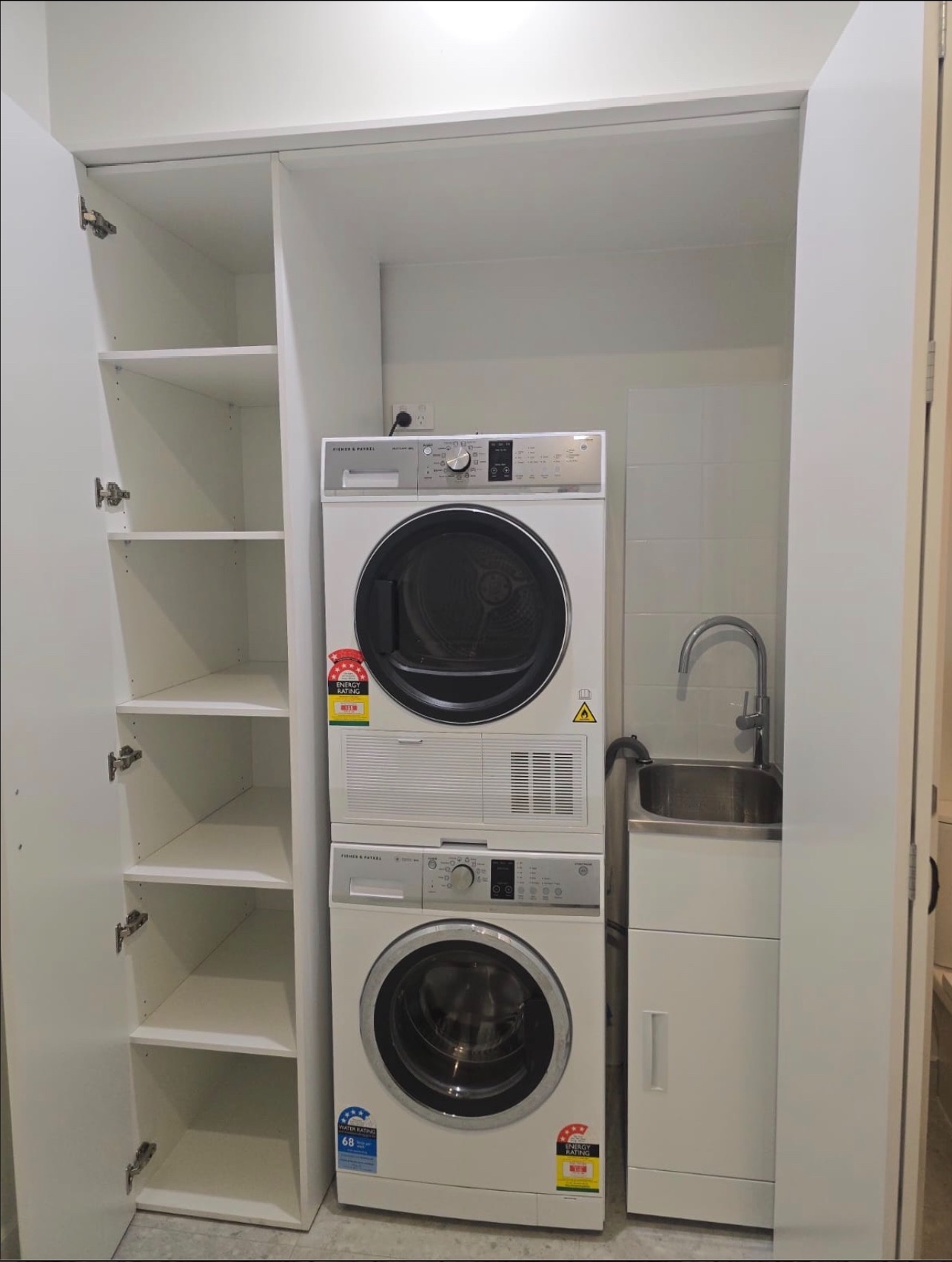 Completed concealed laundry with stacked appliances, sink and open storage — Clayton