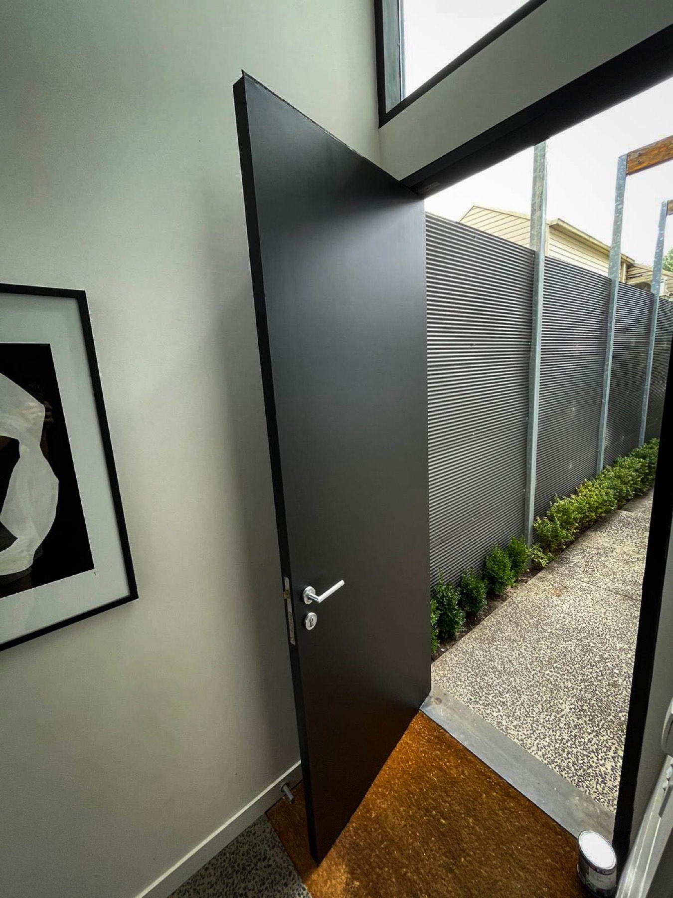 Oversized black pivot entrance door operating within the existing frame